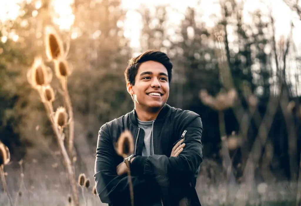 Smiling young man in dark jacket standing in dried field at sunset.