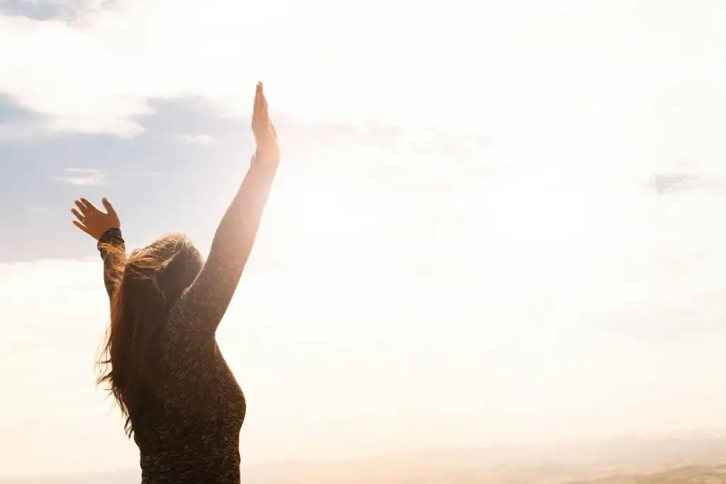 Woman with arms raised celebrating against bright sky and clouds.