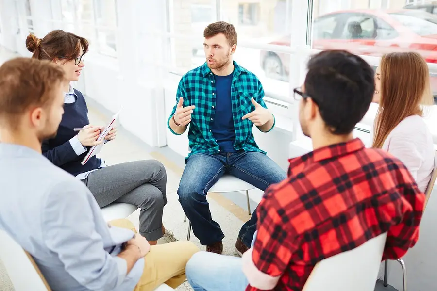 Group of adults sitting in circle during support group meeting or counseling session.