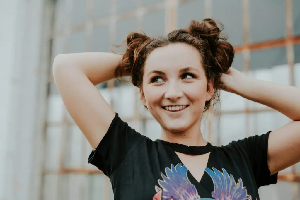 Young woman smiling with hands behind head wearing black graphic tee.