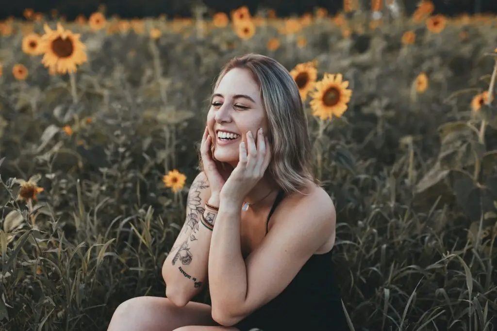 Woman smiling in sunflower field, expressing joy and wellness.