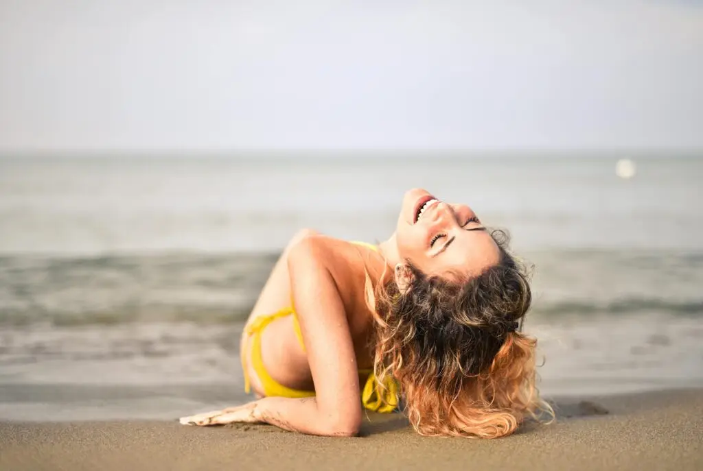 Woman in yellow bikini relaxing joyfully on beach sand by ocean.