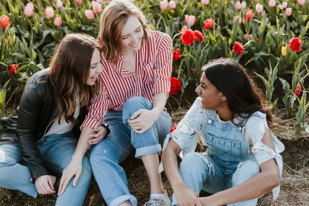 Three young women sitting together in a colorful tulip field, smiling and conversing.