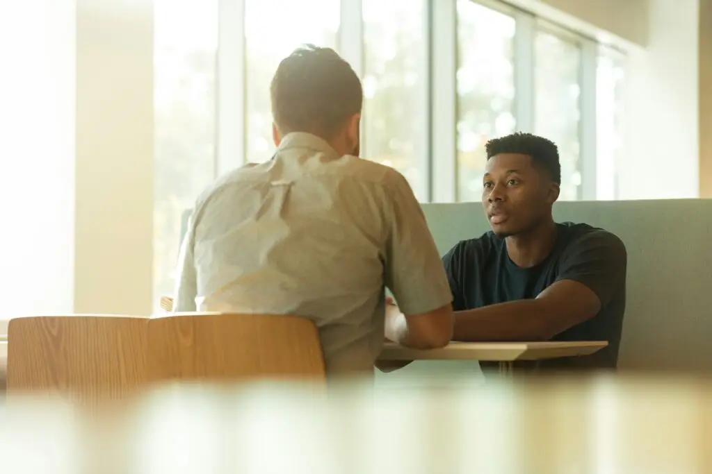 Two men in counseling session at bright, modern facility with large windows.