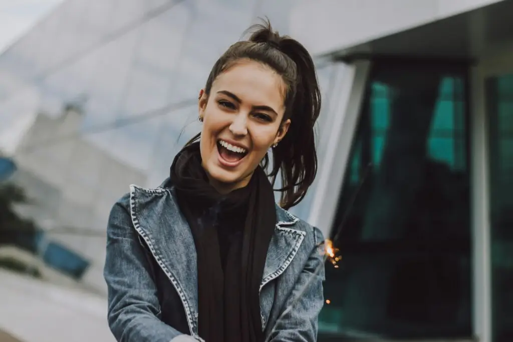 Young woman smiling outdoors wearing denim jacket and black scarf.