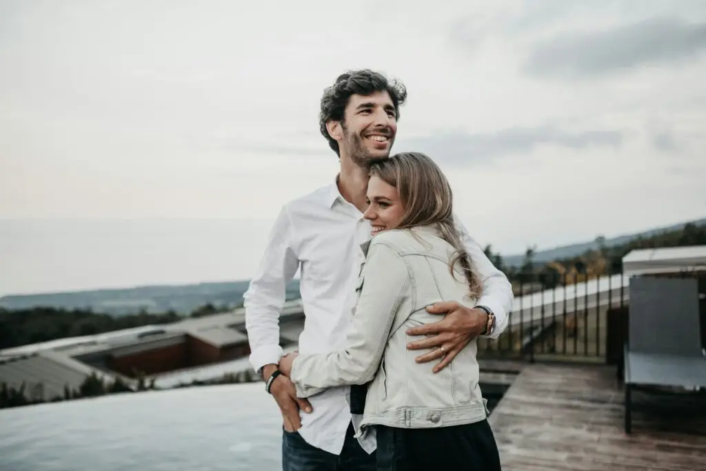 Happy couple embracing on rooftop terrace overlooking scenic landscape.