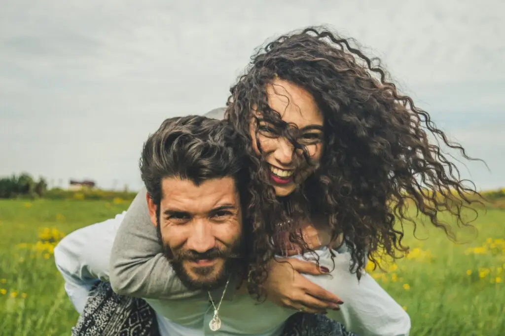 Smiling couple embracing outdoors in green field on sunny day.