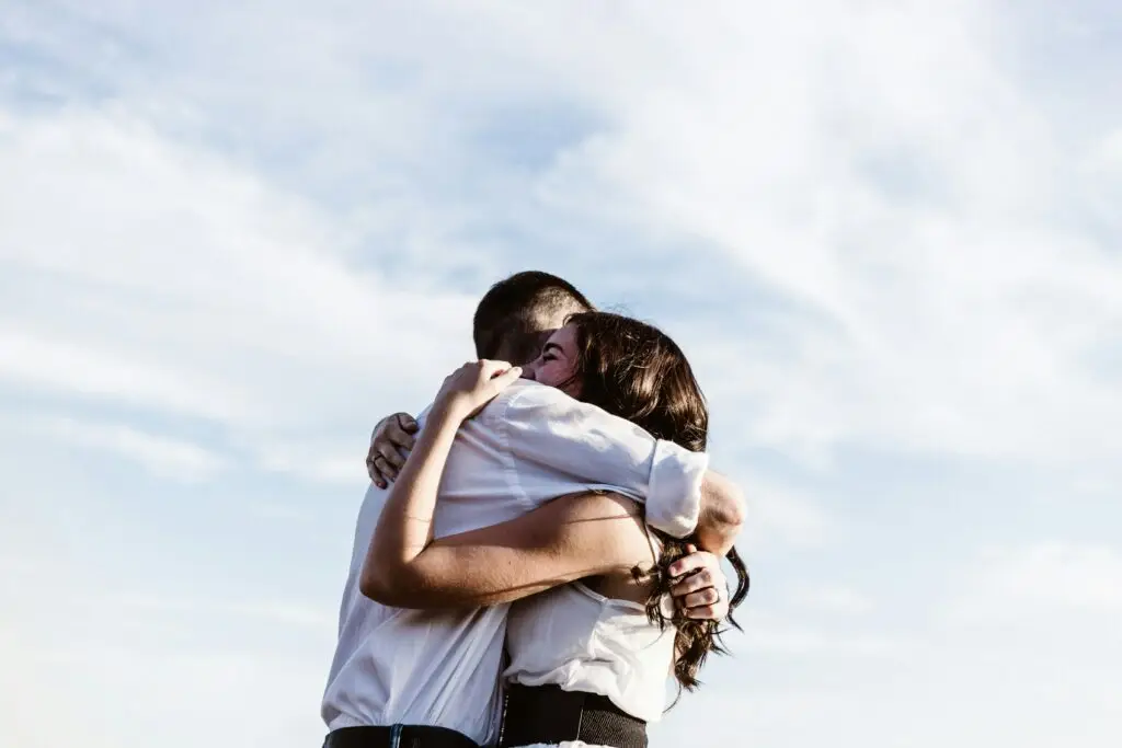 Man embracing woman outdoors against blue sky, showing emotional support and connection.