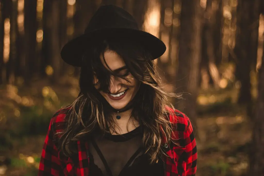 Woman smiling in forest wearing red plaid shirt and black hat.