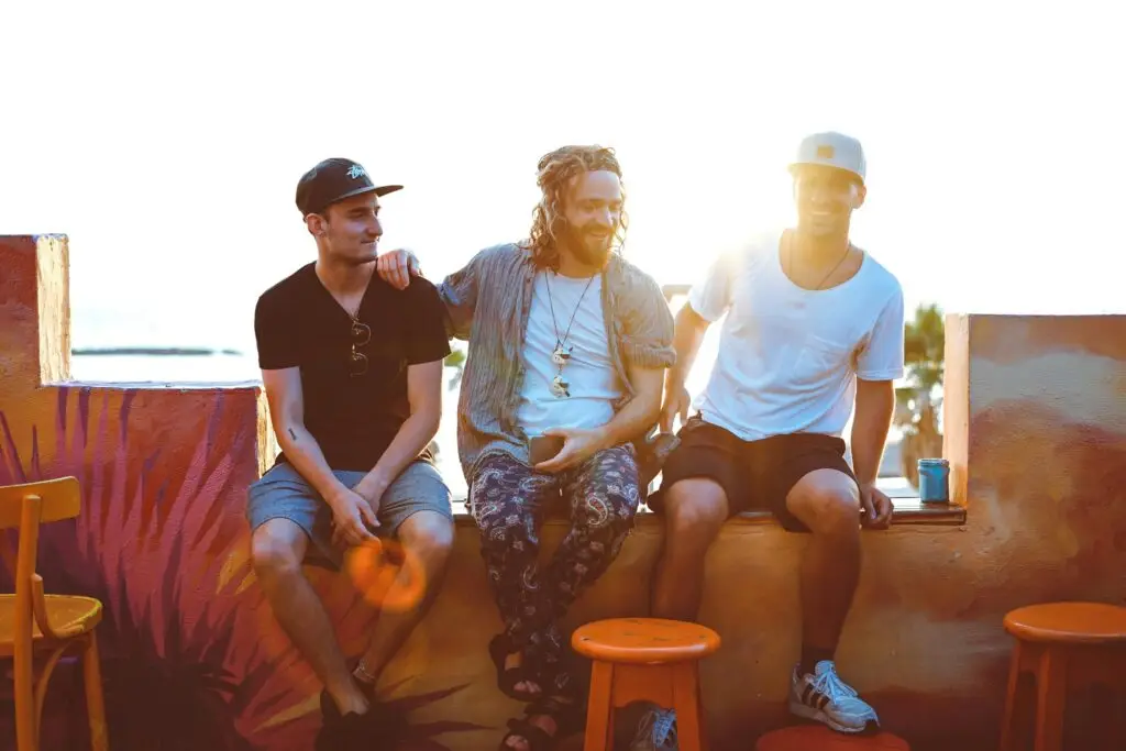 Three men sitting together outdoors during sunset, appearing relaxed and conversational.
