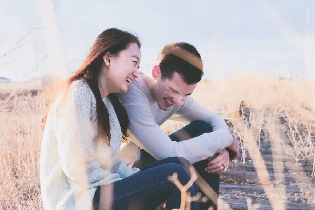 Happy couple laughing together in a sunny rural field during golden hour.