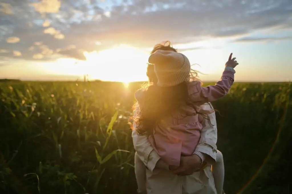 Adult holding child in cornfield at sunset, celebrating recovery and hope.