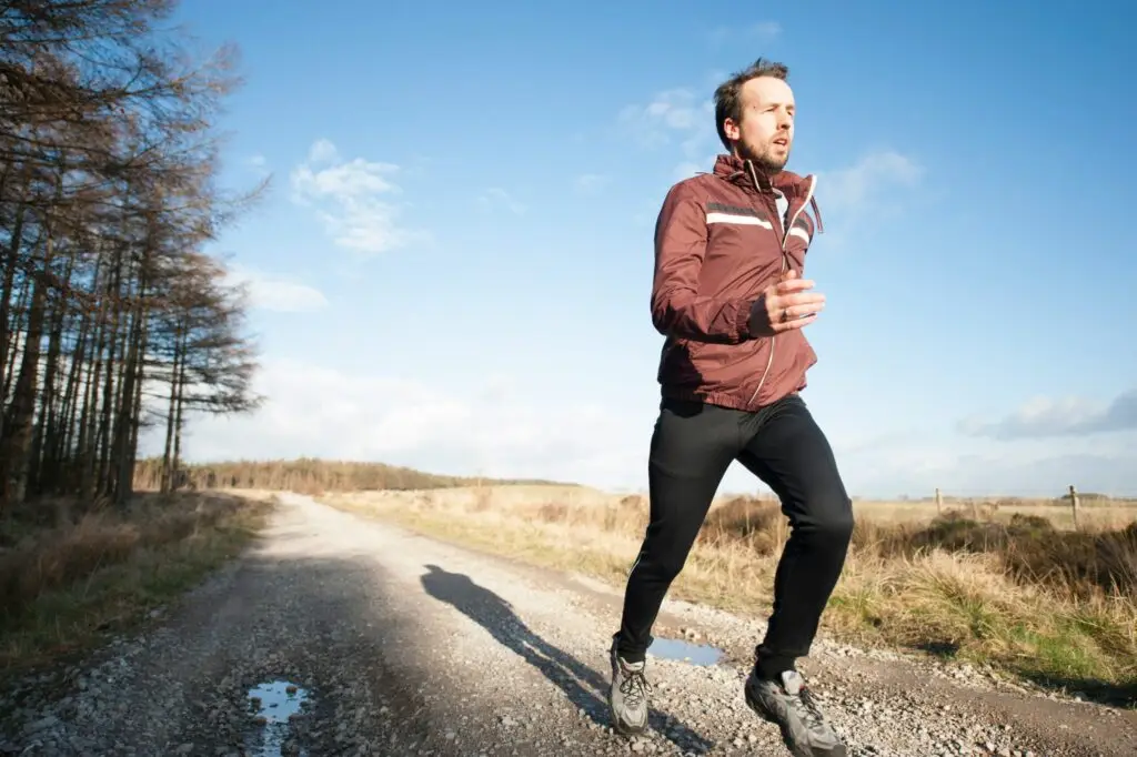 Man jogging on rural dirt road on sunny day with bare trees.